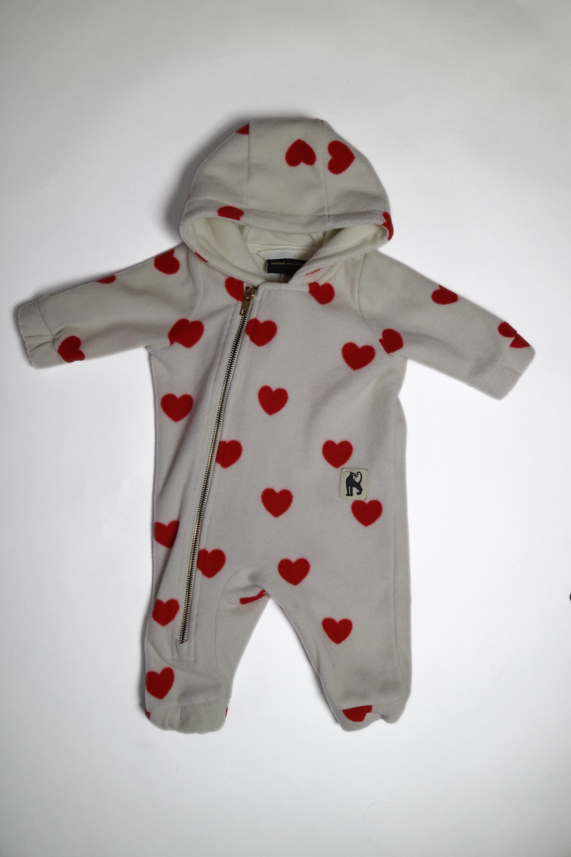 Fleece-onesie med heltäckande Hearts-print tillverkad i 100 % återvunnen polyester, fodrad med fleece, från Mini Rodini. Onesien har dragkedja från hals till benslut och Mini Rodinis klassiska Panther-märke framtill. 