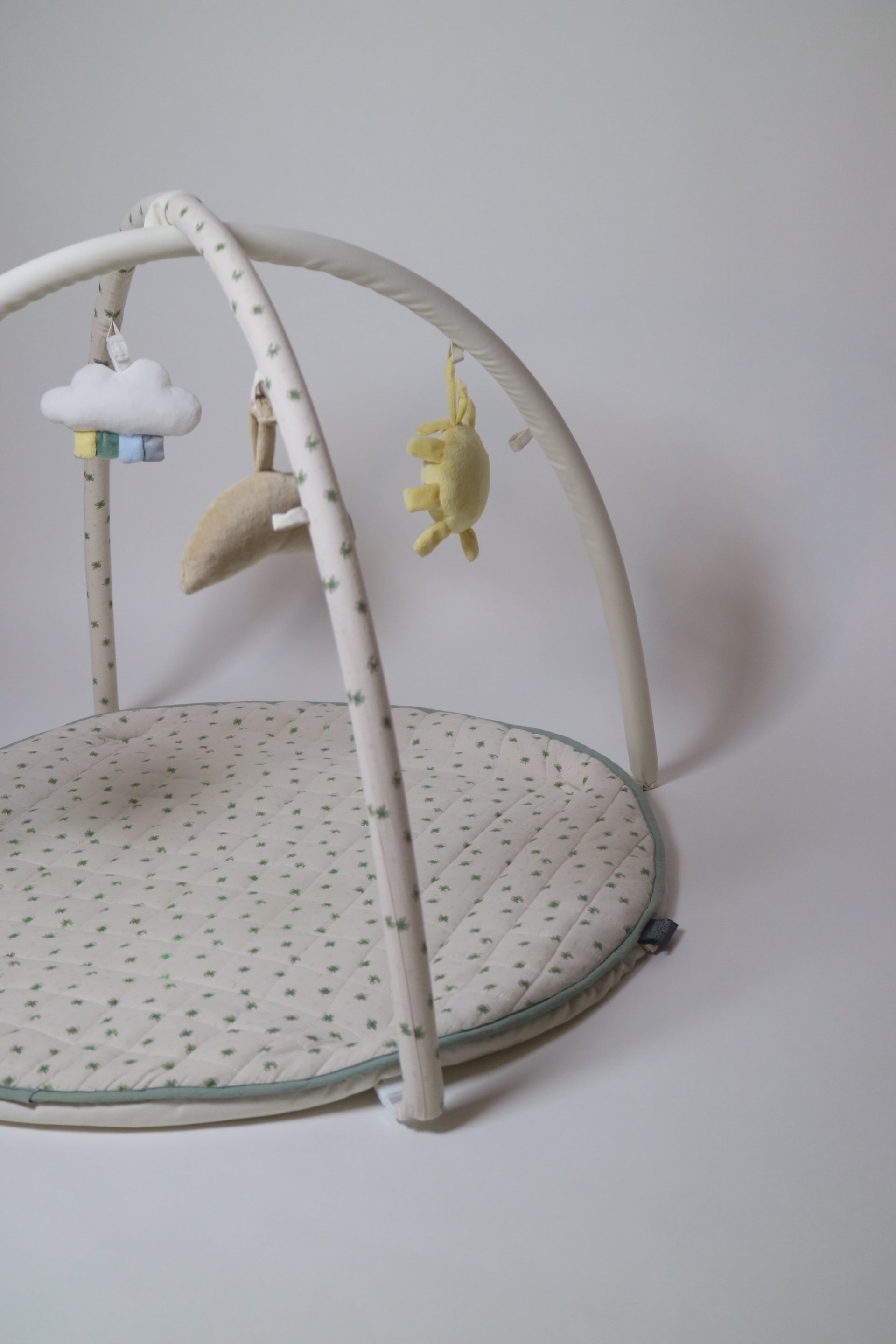 Babygym i modell Meadow från Vinter &amp; Bloom. Den quiltade mattan är vit med gröna blommor/klöver och kan även användas som lekmatta genom att ta av bågarna.  sidan.