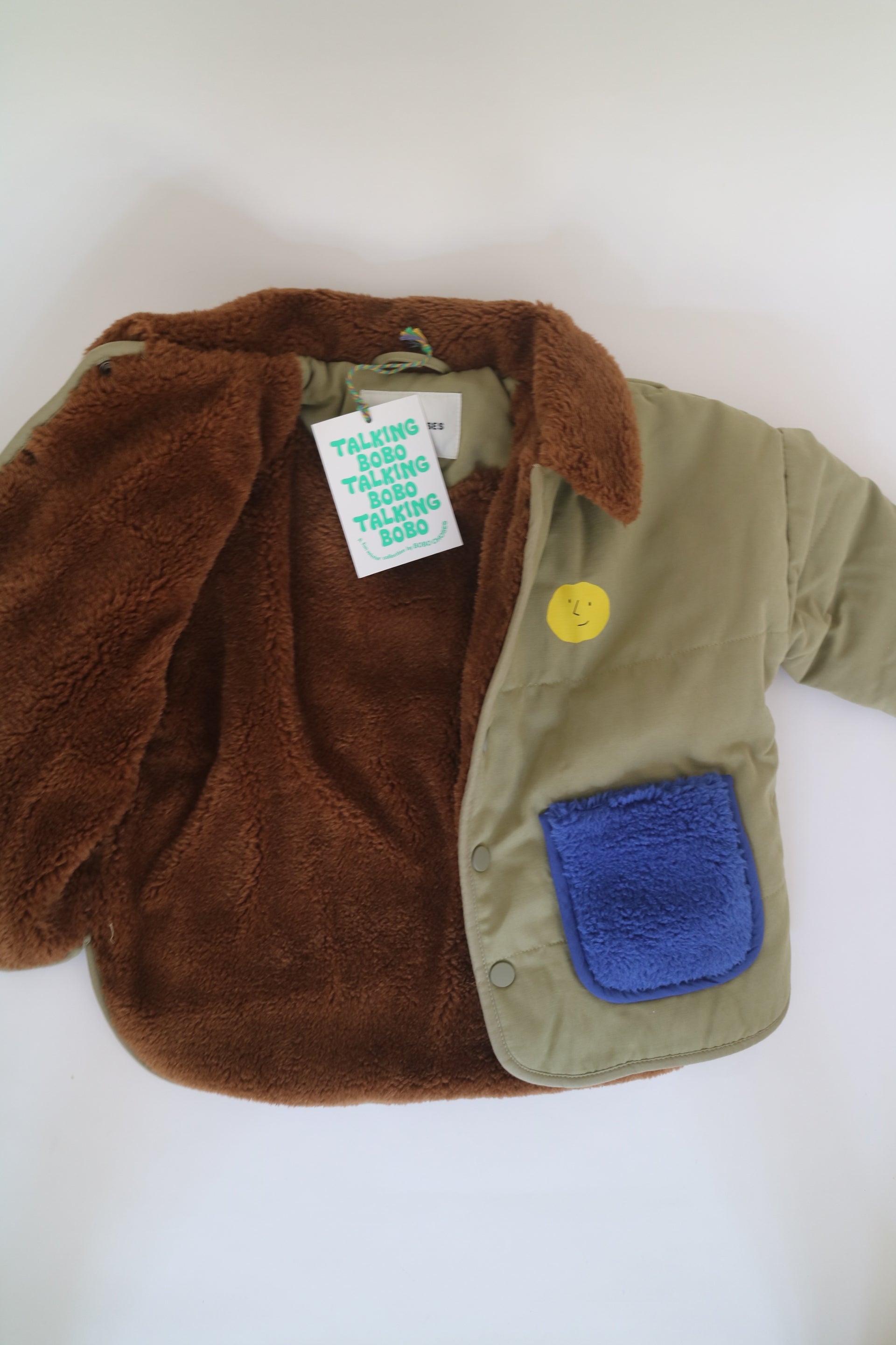 Fodrad jacka i ljus militärgrön färg med kornblåa fickor och brun krage i teddy-material från Bobo Choses, modell Face Multicolor Jacket.2