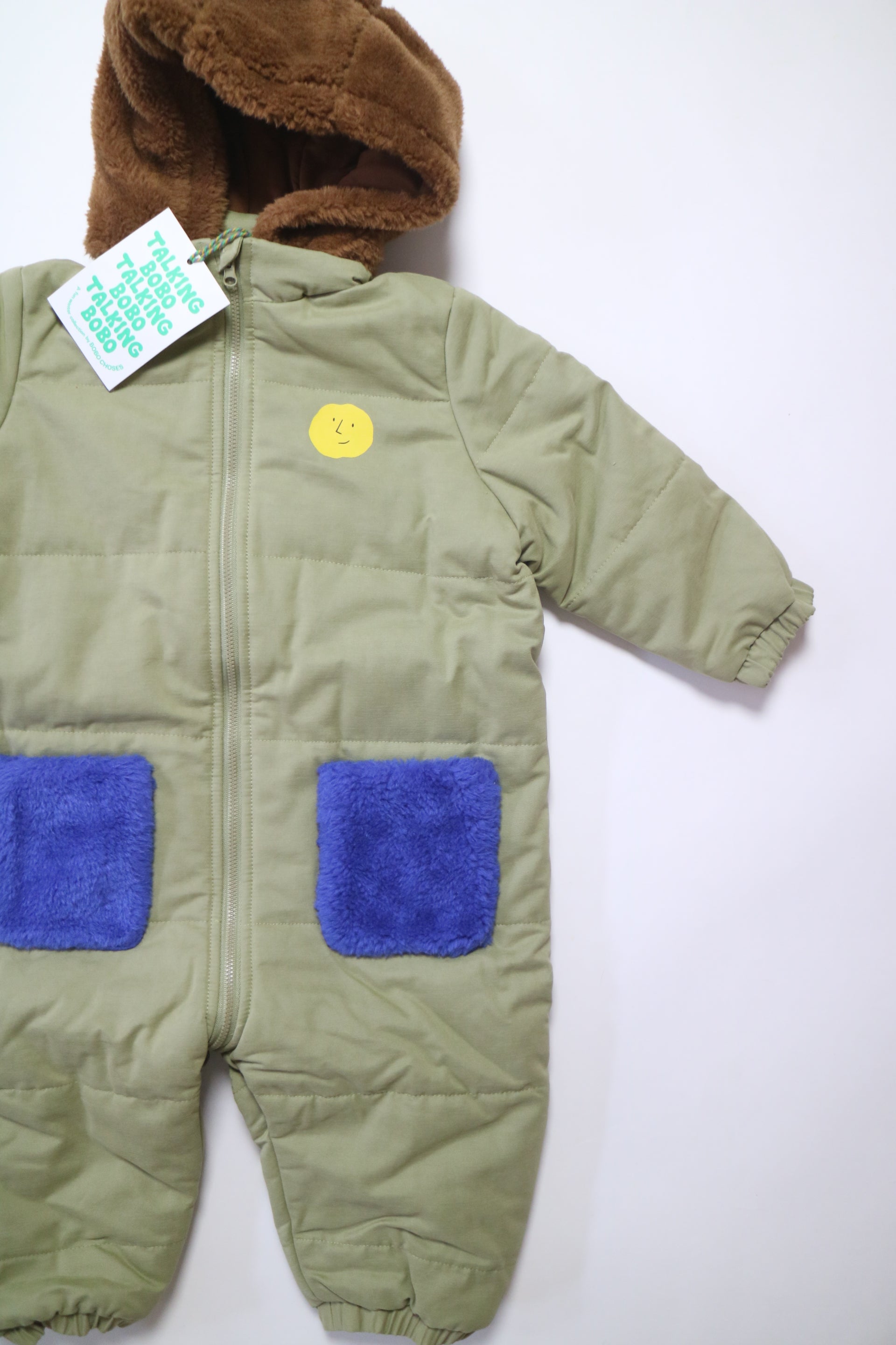 Fodrad overall i ljus militärgrön färg med kornblåa fickor och brun luva i teddy-material från Bobo Choses, modell Face Multicolor Overall.2