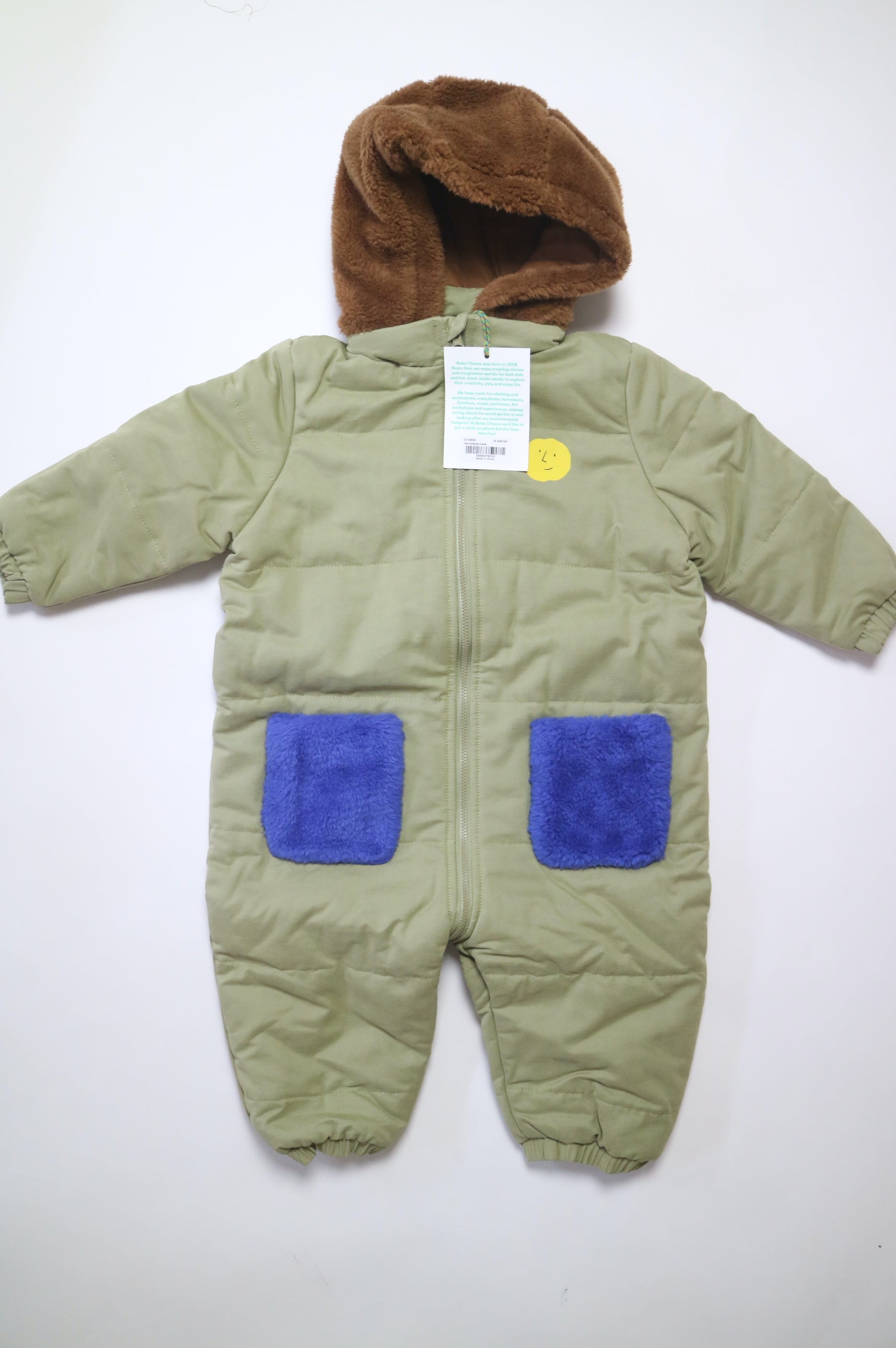 Fodrad overall i ljus militärgrön färg med kornblåa fickor och brun luva i teddy-material från Bobo Choses, modell Face Multicolor Overall.