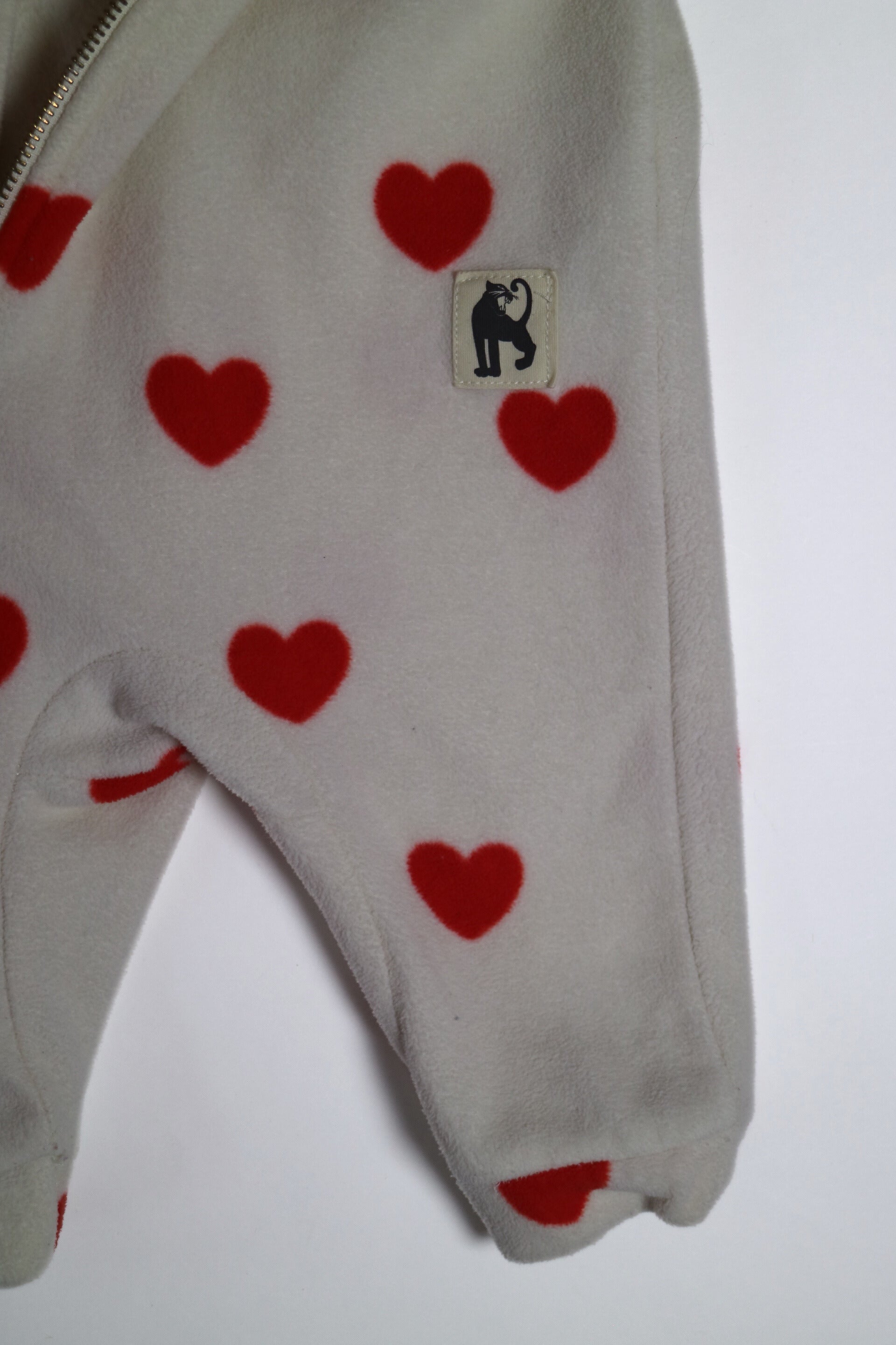 Fleece-onesie med heltäckande Hearts-print tillverkad i 100 % återvunnen polyester, fodrad med fleece, från Mini Rodini. Onesien har dragkedja från hals till benslut och Mini Rodinis klassiska Panther-märke framtill. 