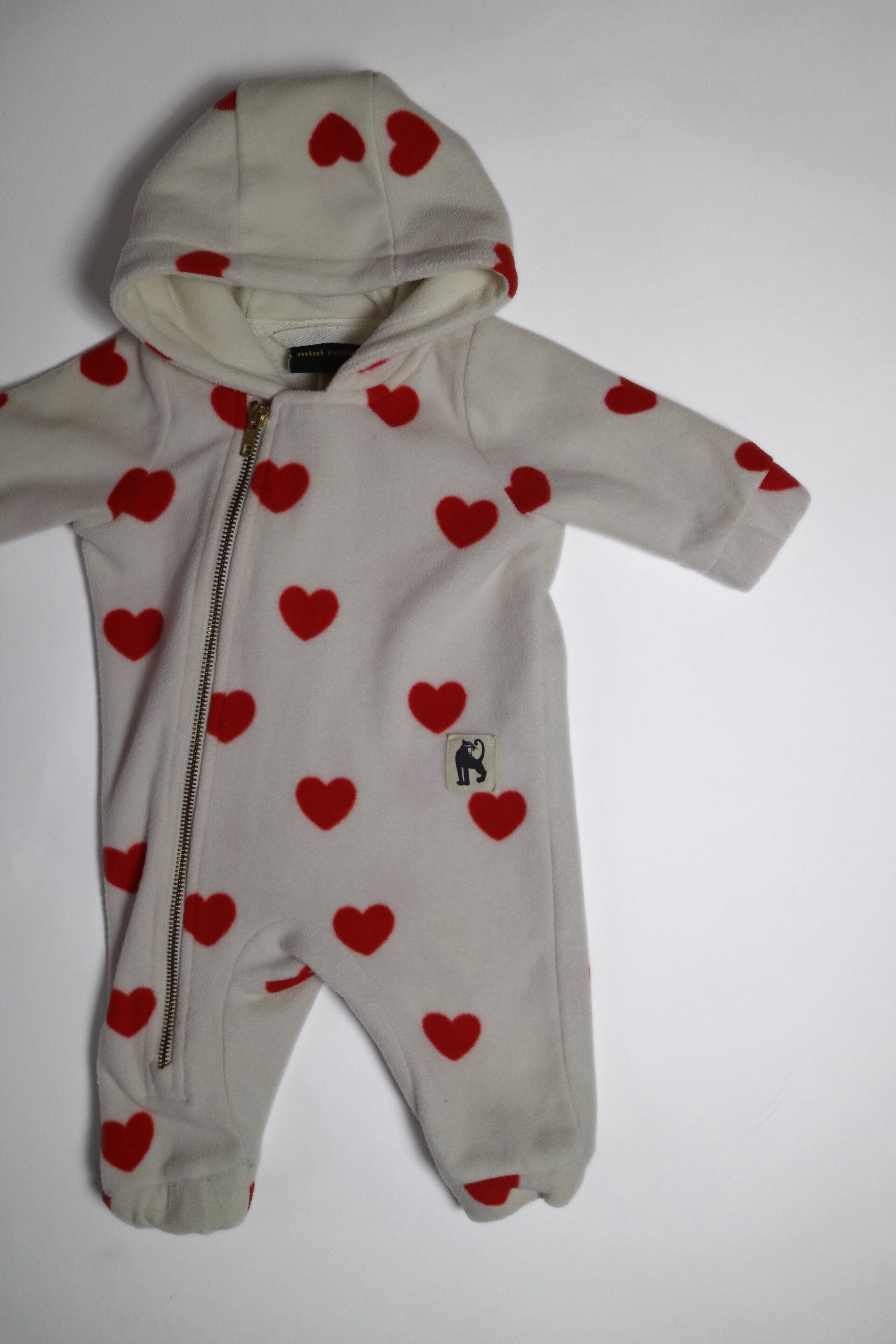 Fleece-onesie med heltäckande Hearts-print tillverkad i 100 % återvunnen polyester, fodrad med fleece, från Mini Rodini. Onesien har dragkedja från hals till benslut och Mini Rodinis klassiska Panther-märke framtill. 