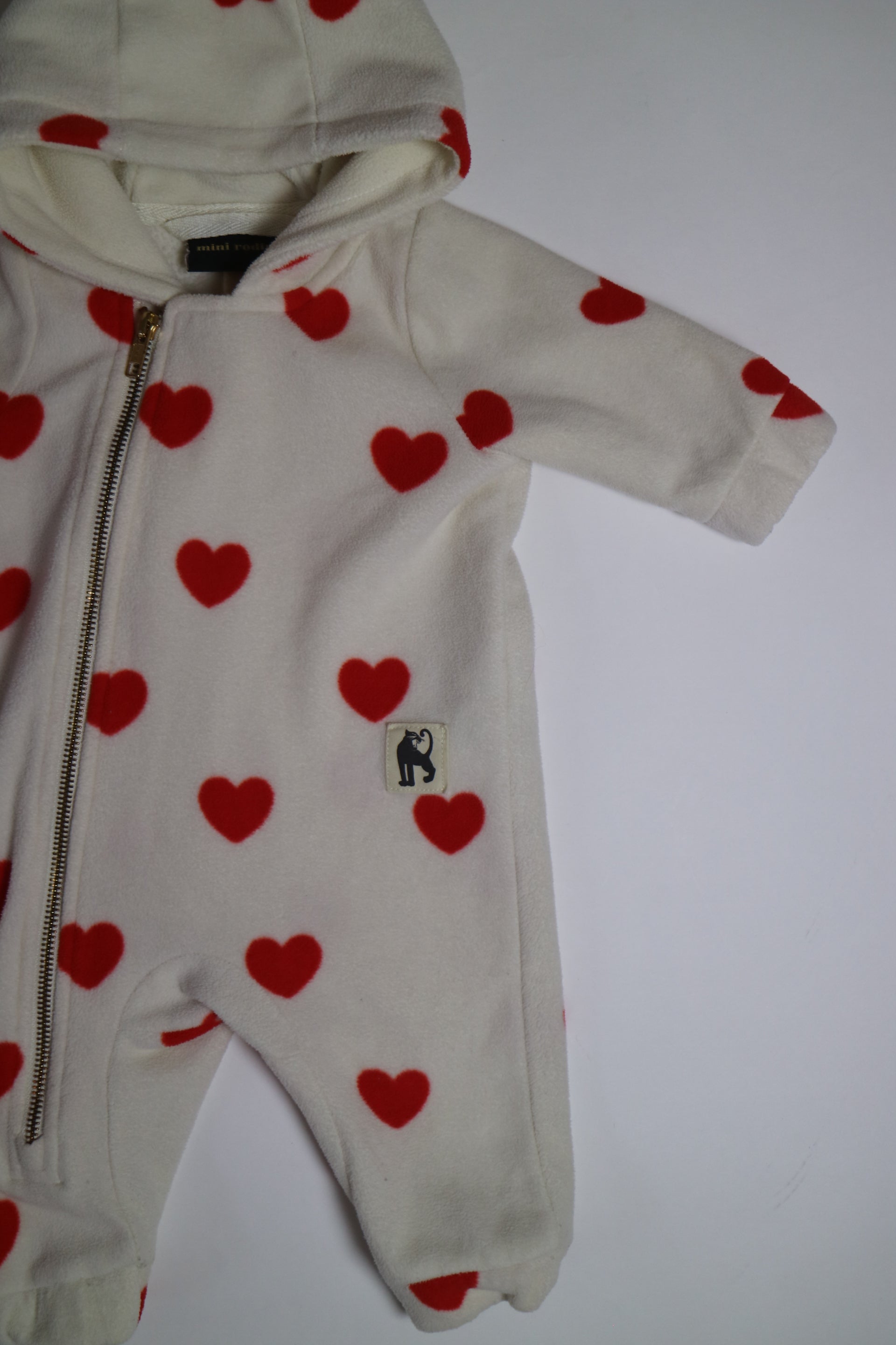 Fleece-onesie med heltäckande Hearts-print tillverkad i 100 % återvunnen polyester, fodrad med fleece, från Mini Rodini. Onesien har dragkedja från hals till benslut och Mini Rodinis klassiska Panther-märke framtill. 